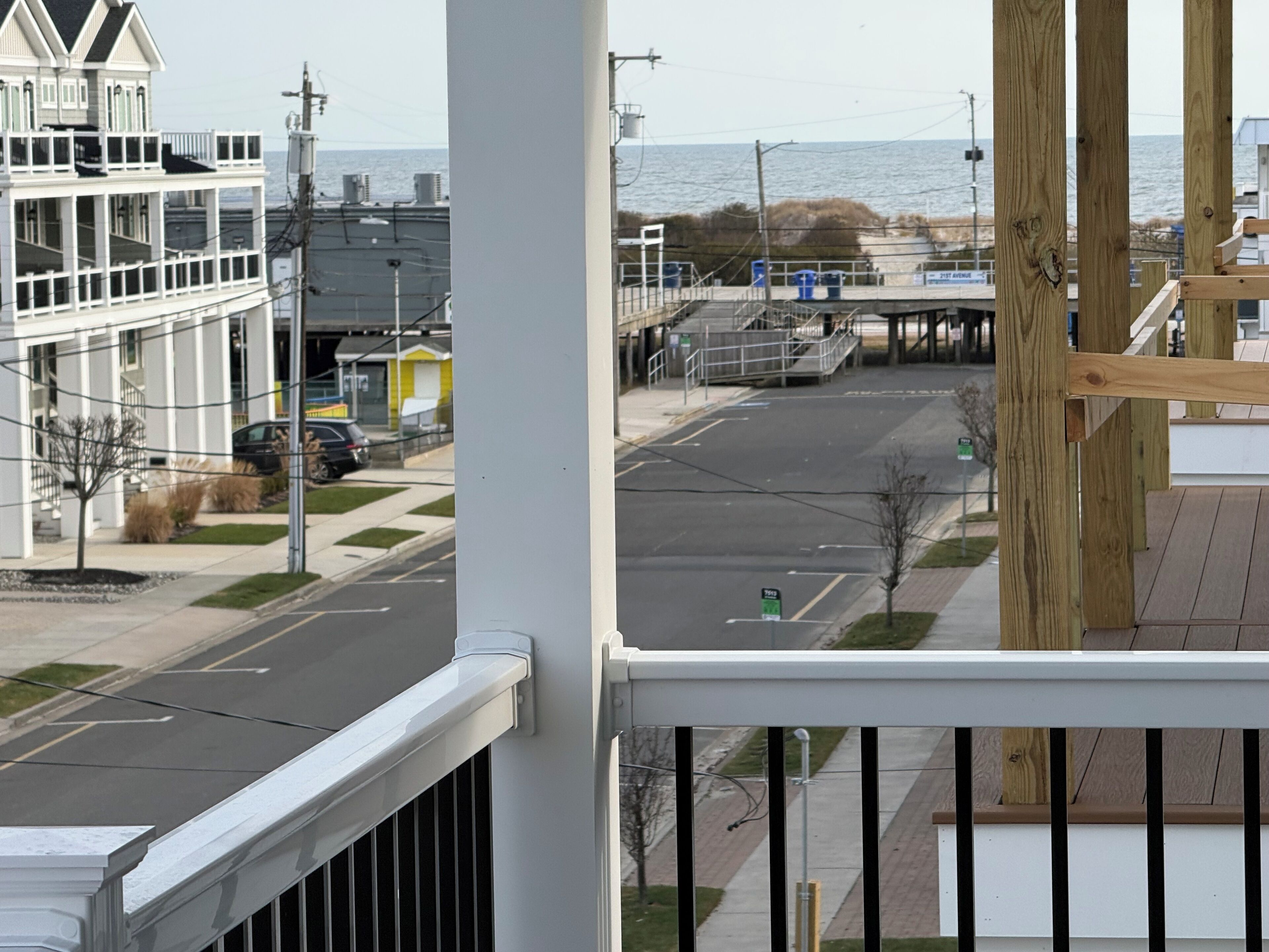 A view from a balcony overlooking a street with a building and a body of water in the background.