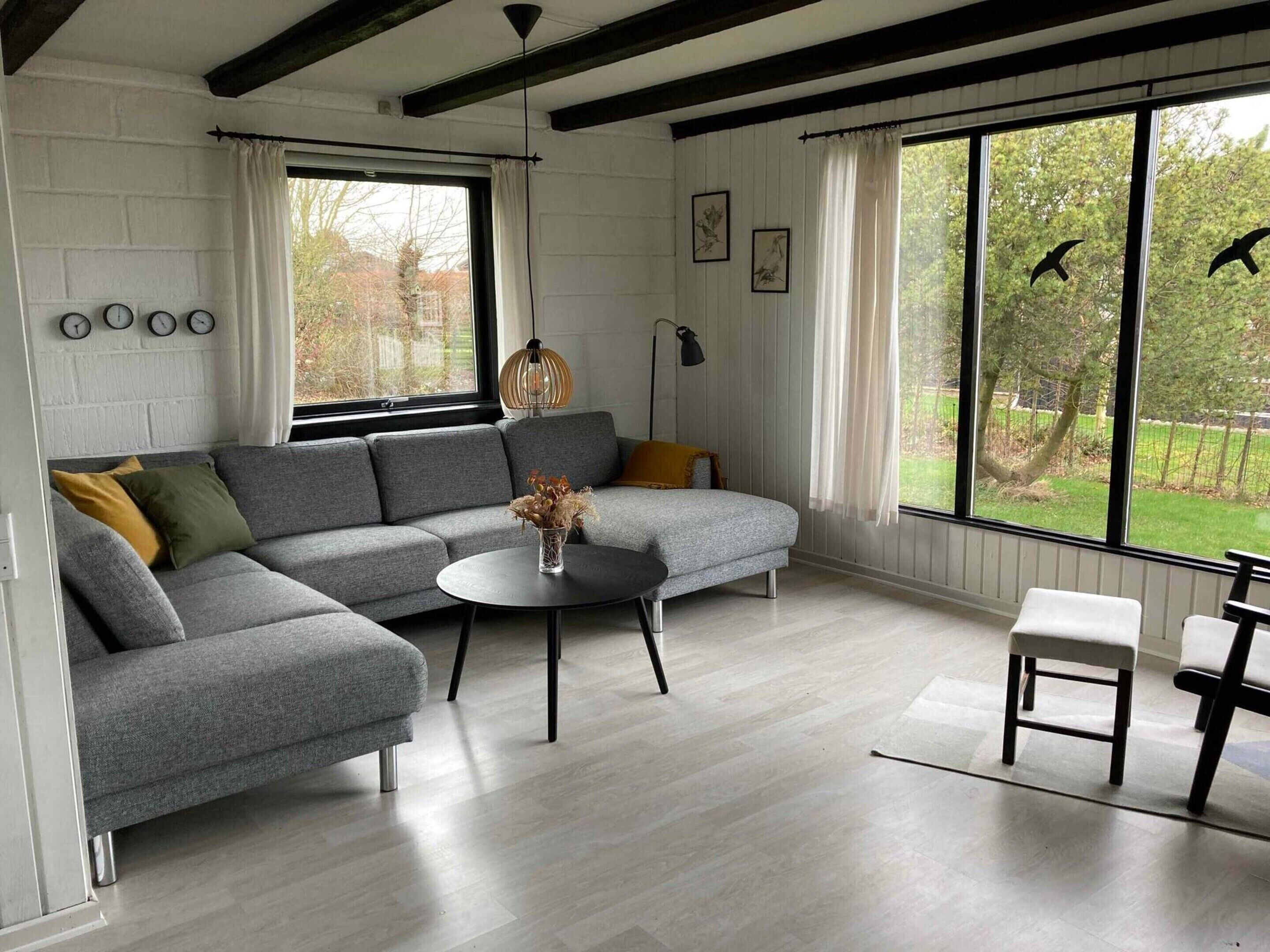 A modern living room with a grey sectional sofa, a round coffee table, and a view of the outdoors through large windows.