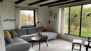 Una sala de estar moderna con un sofá seccional gris, una mesa redonda de centro y vistas al exterior a través de amplios ventanales.