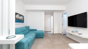 A modern living room with a teal sectional sofa, a flat-screen TV mounted on the wall, and a painting on the wall. - Amal & Surya apartments (Sorrento)