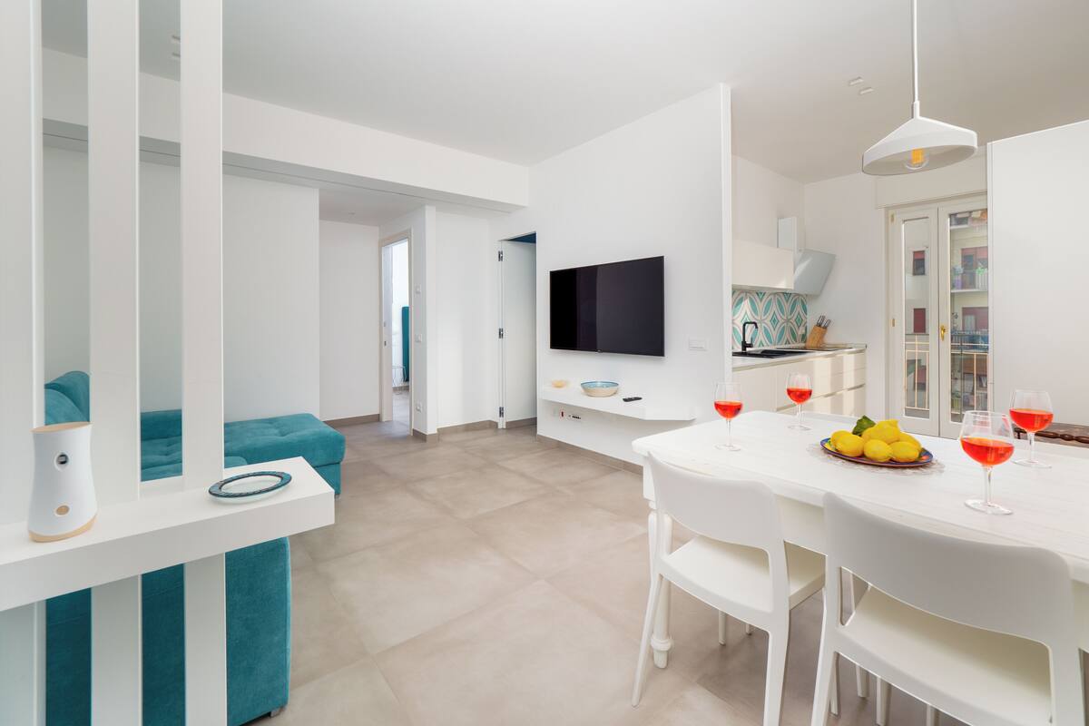 A modern kitchen with a dining area, white furniture, and a flat-screen TV.