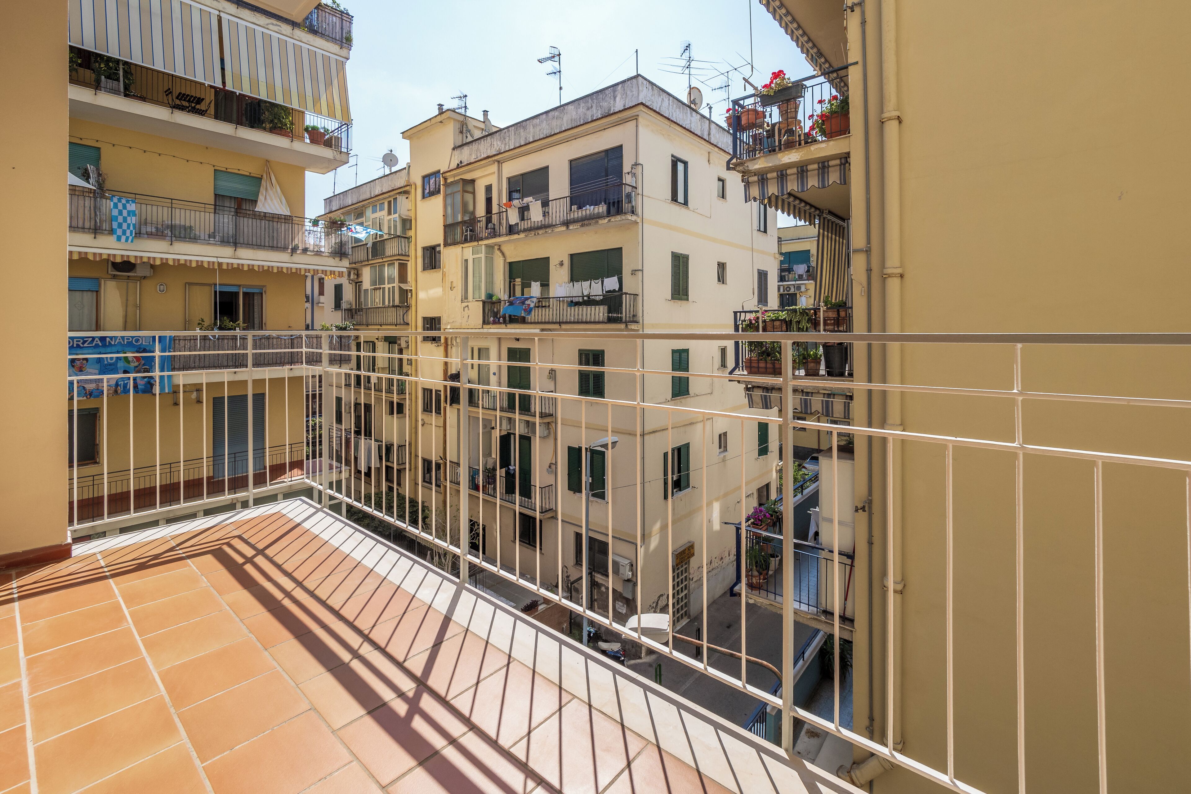 A multi-story residential building with balconies, a tiled terrace, and a visible sign for "ORZA NAPOLI".