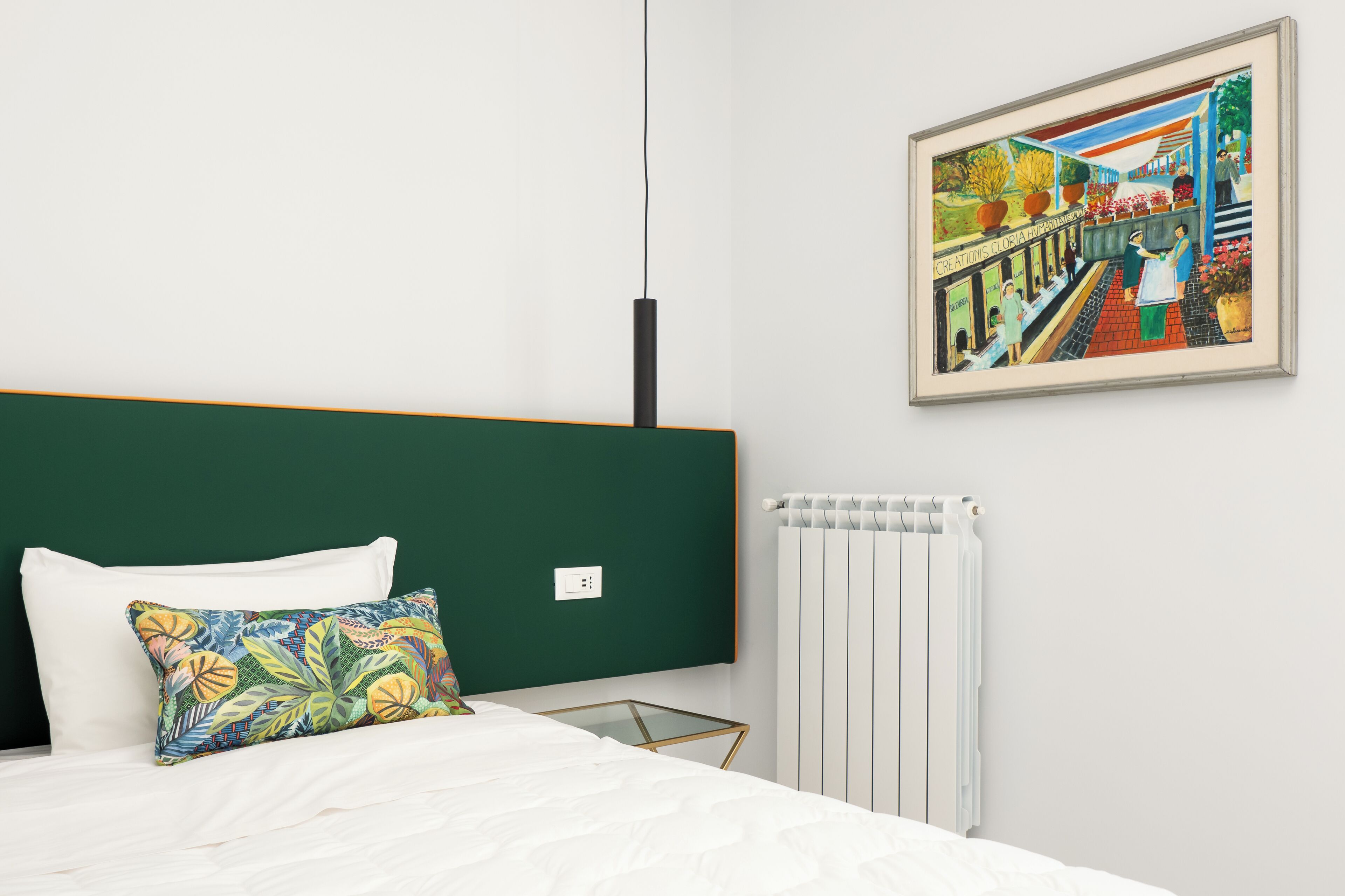 A bedroom with a bed, a green headboard, a white radiator, and a framed painting on the wall.