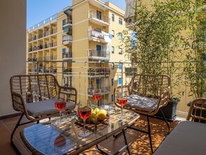 A balcony with wicker chairs, a glass table, and potted plants. - Amal & Surya apartments (Sorrento)