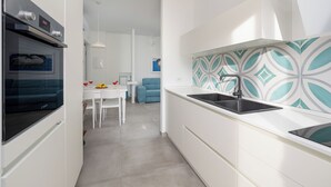 A modern kitchen with white cabinetry, a black sink, and a patterned backsplash. - Amal & Surya apartments (Sorrento)
