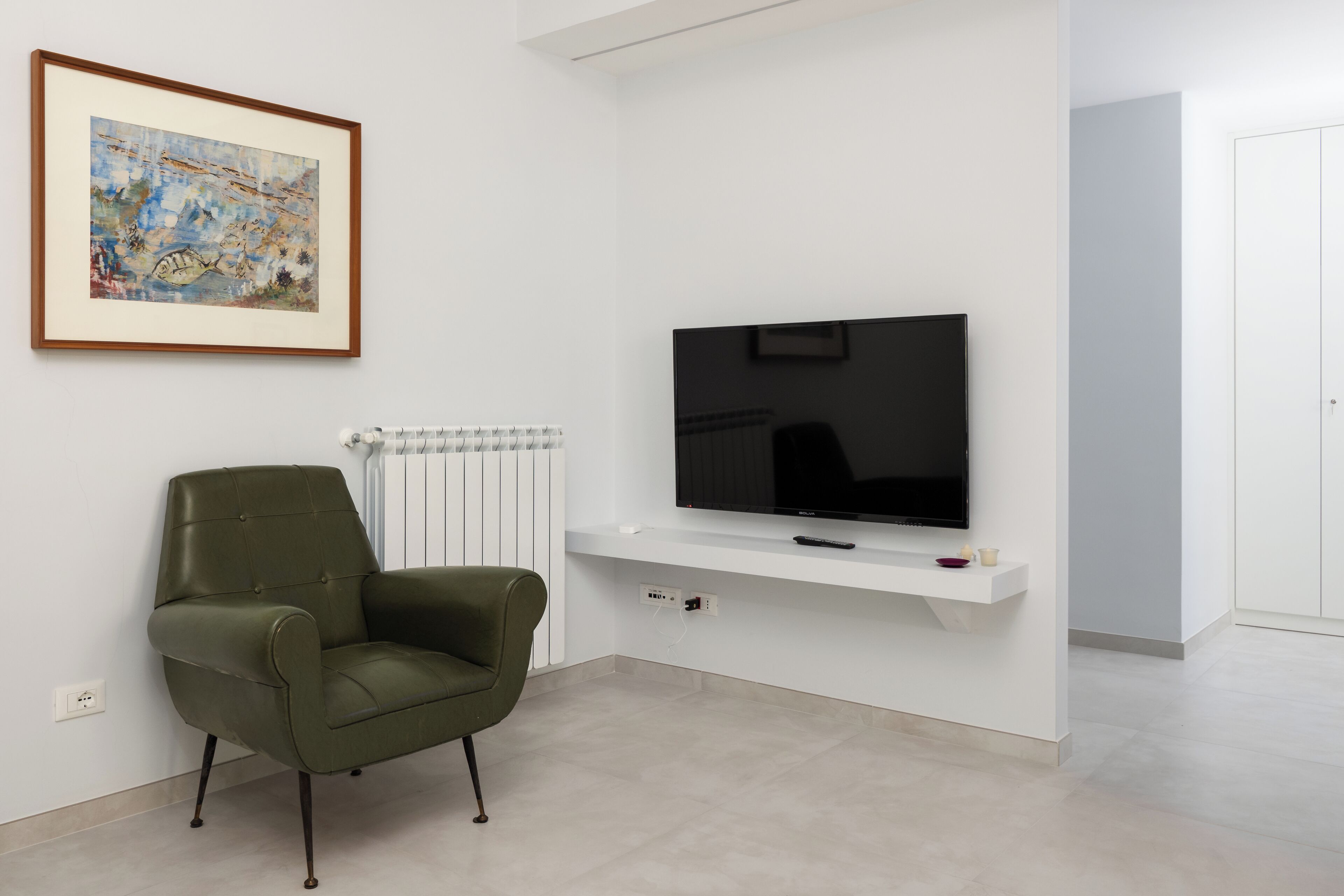 En moderne stue med et fladskærms-tv monteret på en hvid væg, en grøn lænestol og et indrammet kunstværk over tv'et.