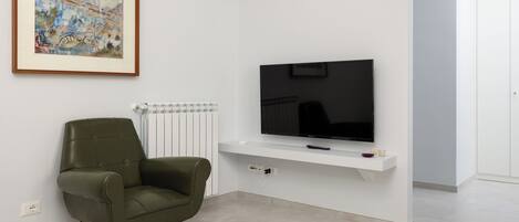 En moderne stue med et fladskærms-tv monteret på en hvid væg, en grøn lænestol og et indrammet kunstværk over tv'et.