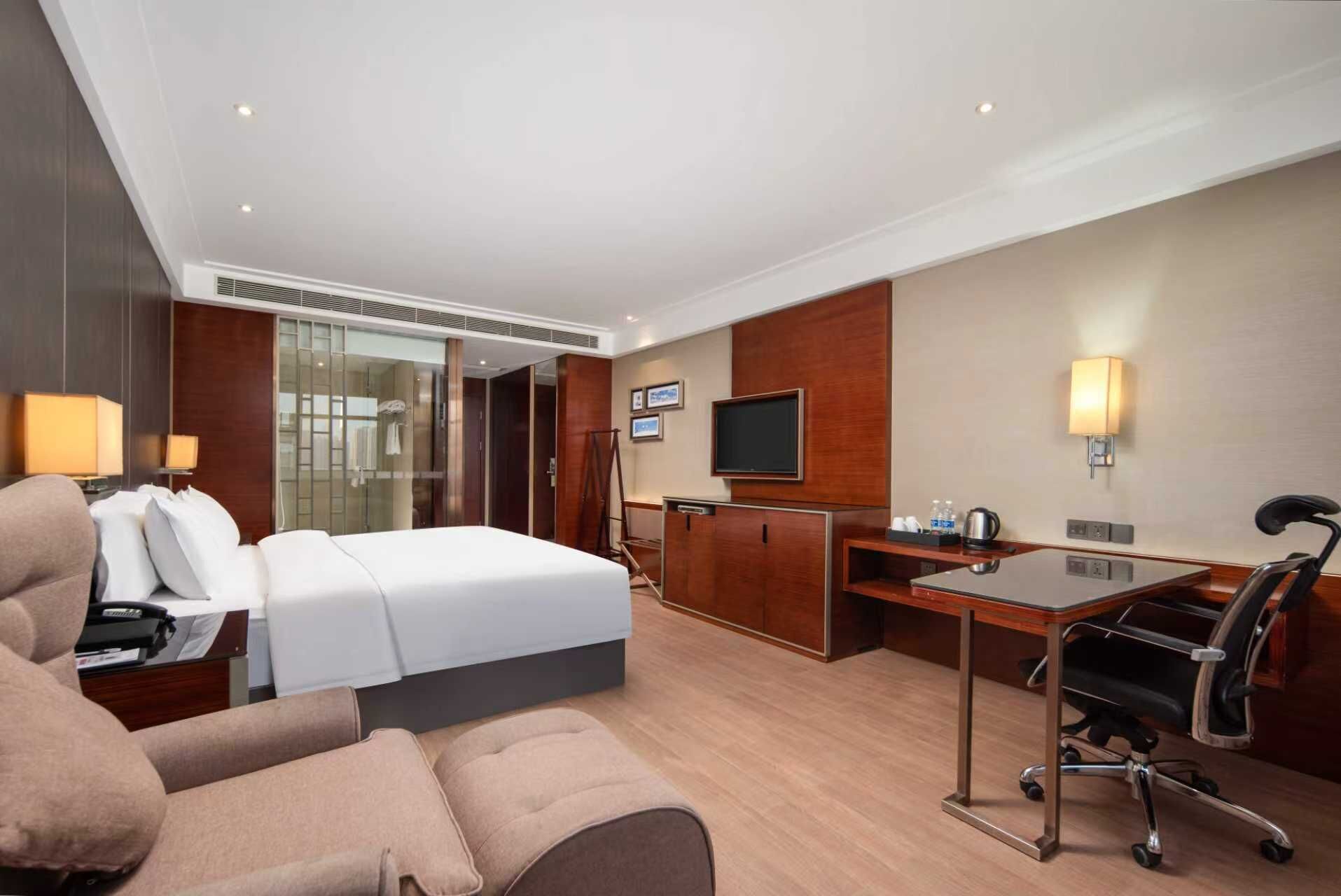 Ett hotellrum med en säng, ett skrivbord, en stol, en TV och en minibar.