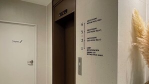 Um saguão de hotel com chão de azulejos brancos, balcão de recepção e um painel fixado na parede listando quartos e comodidades.