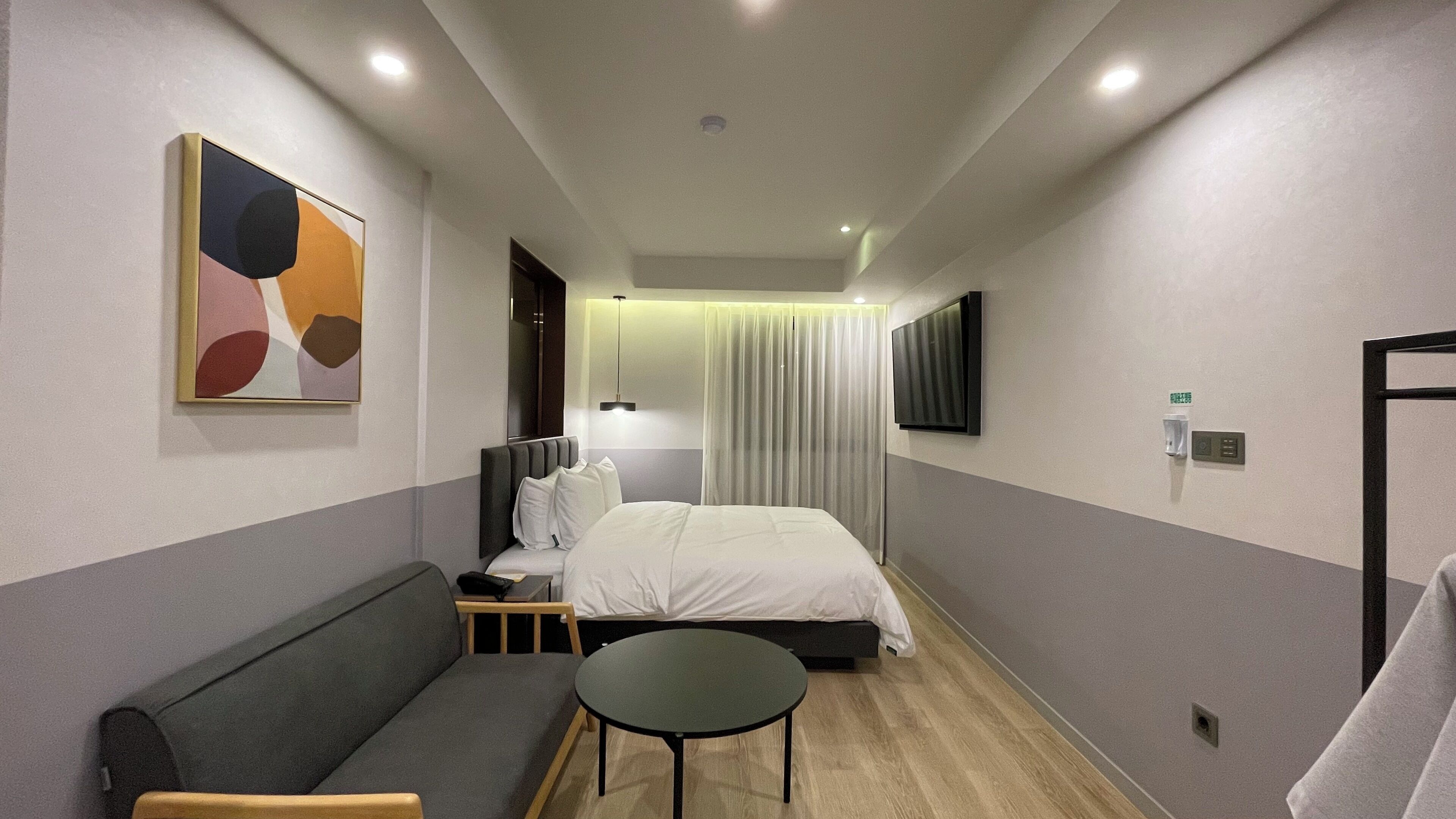 Et hotelværelse med en seng, en sofa, et lille bord, et fjernsyn og et maleri på væggen.