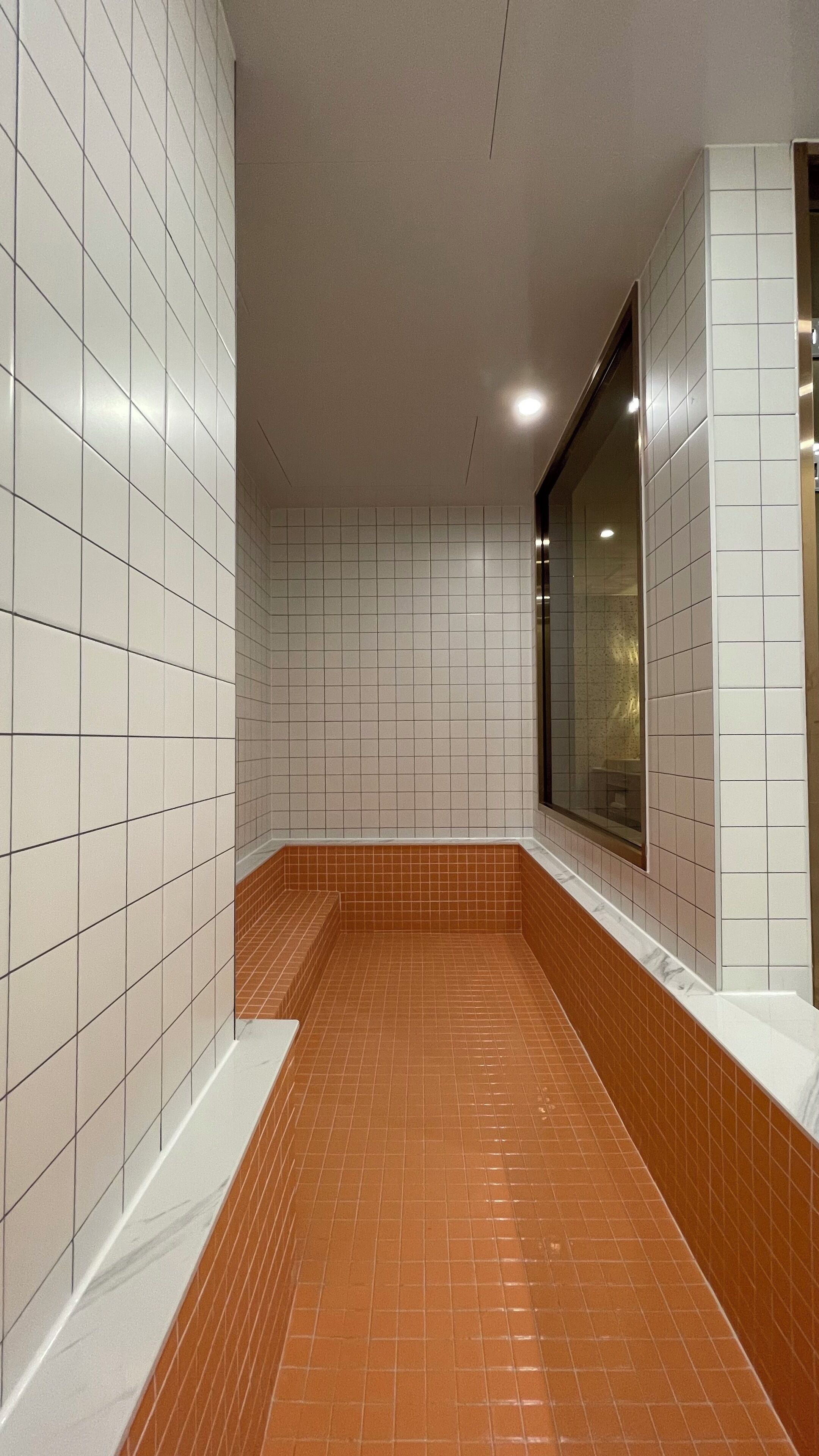 A bathroom with white tiled walls and a brown tiled floor.