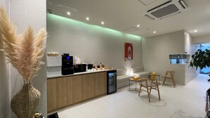 Cozinha moderna com máquina de café, geladeira e área de estar com mesa e cadeiras.