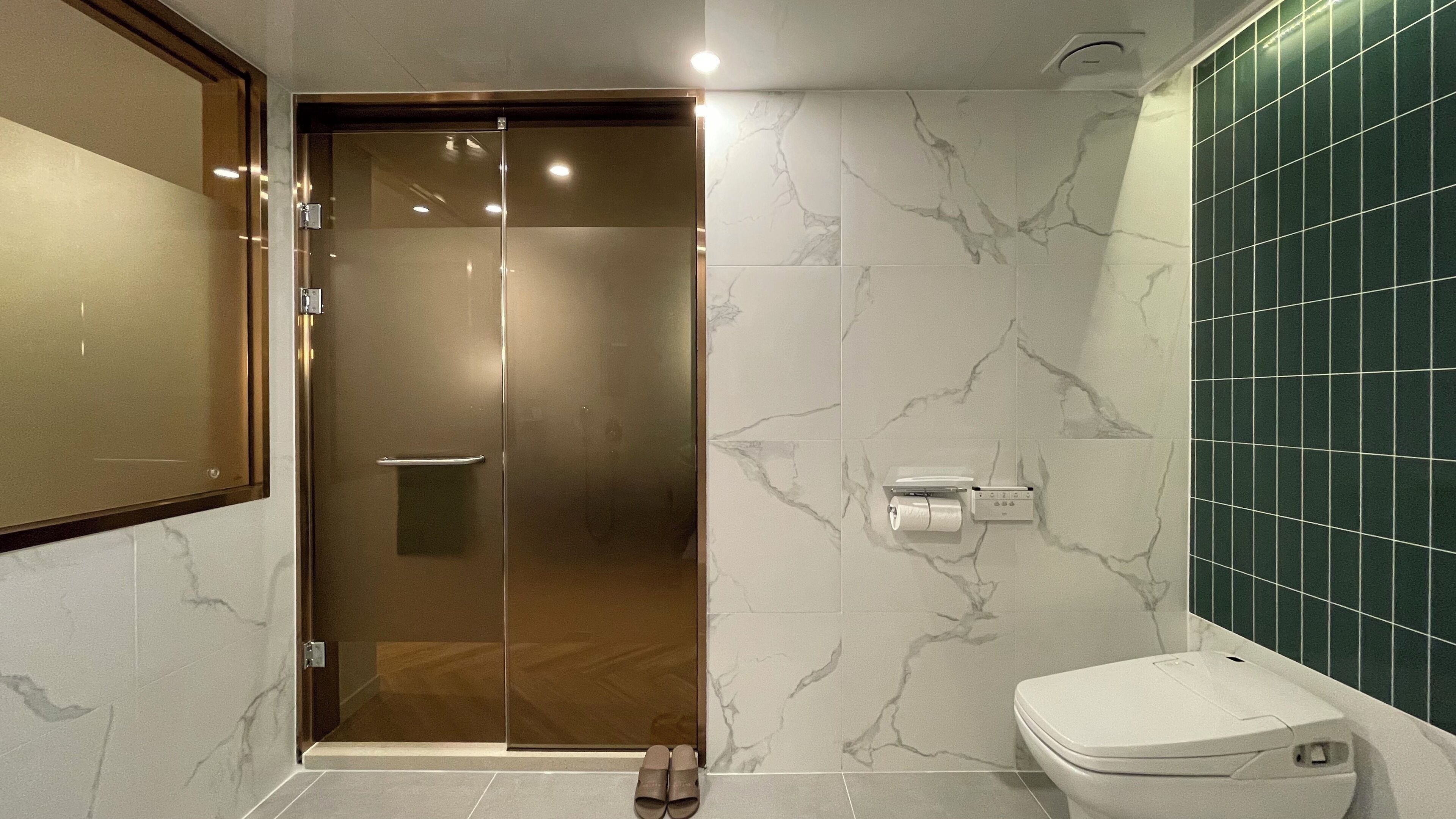 A modern bathroom with a glass shower door, a toilet, and a marble-patterned wall.