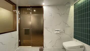 A modern bathroom with a glass shower door, a toilet, and a marble-patterned wall.