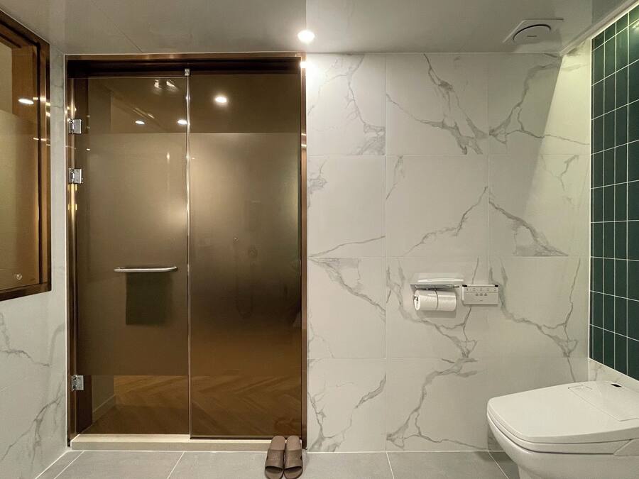 A modern bathroom with a glass shower door, a toilet, and a marble-patterned wall.