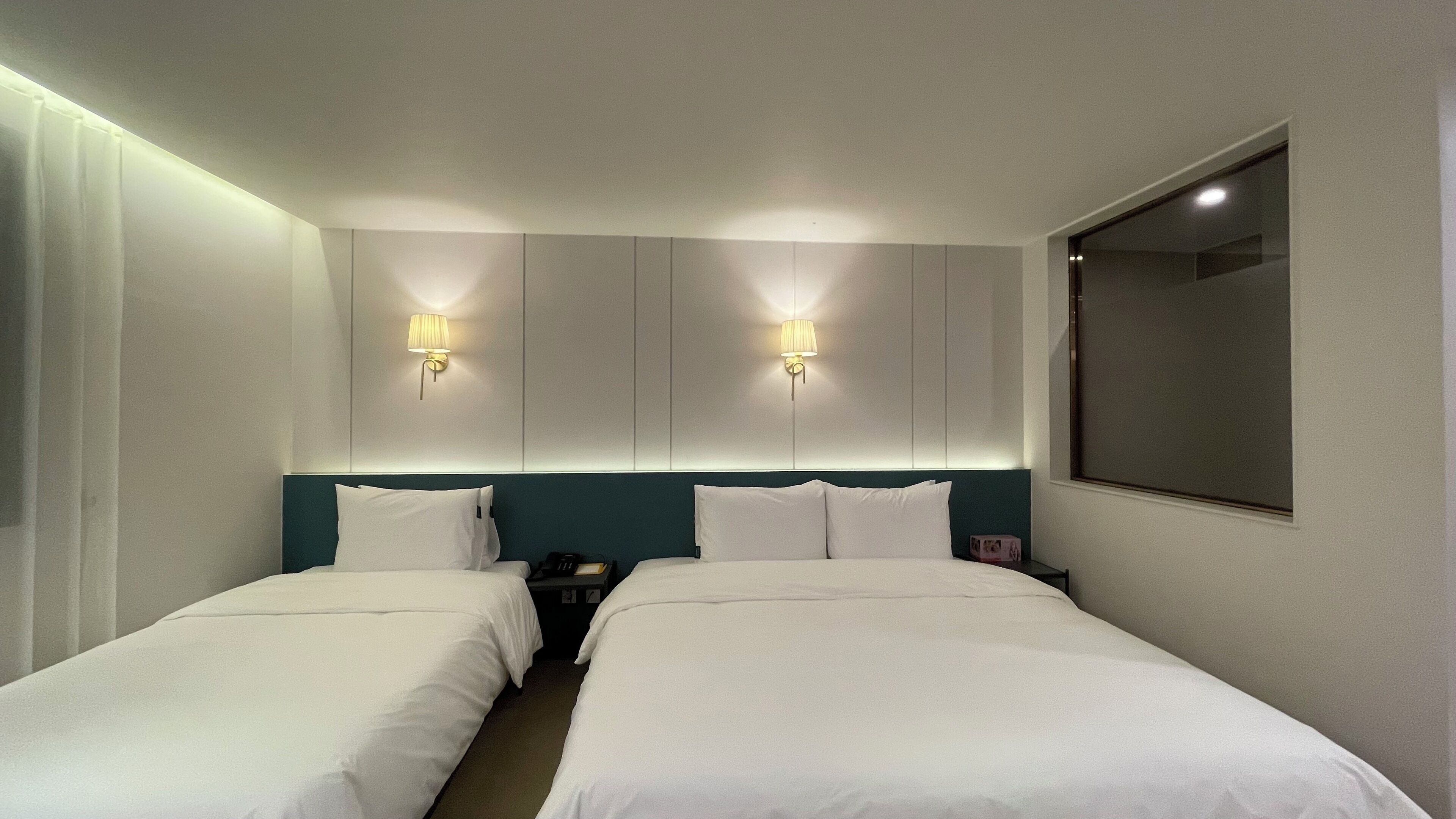 Et hotelværelse med to enkeltsenge, et stort spejl og to væglamper.