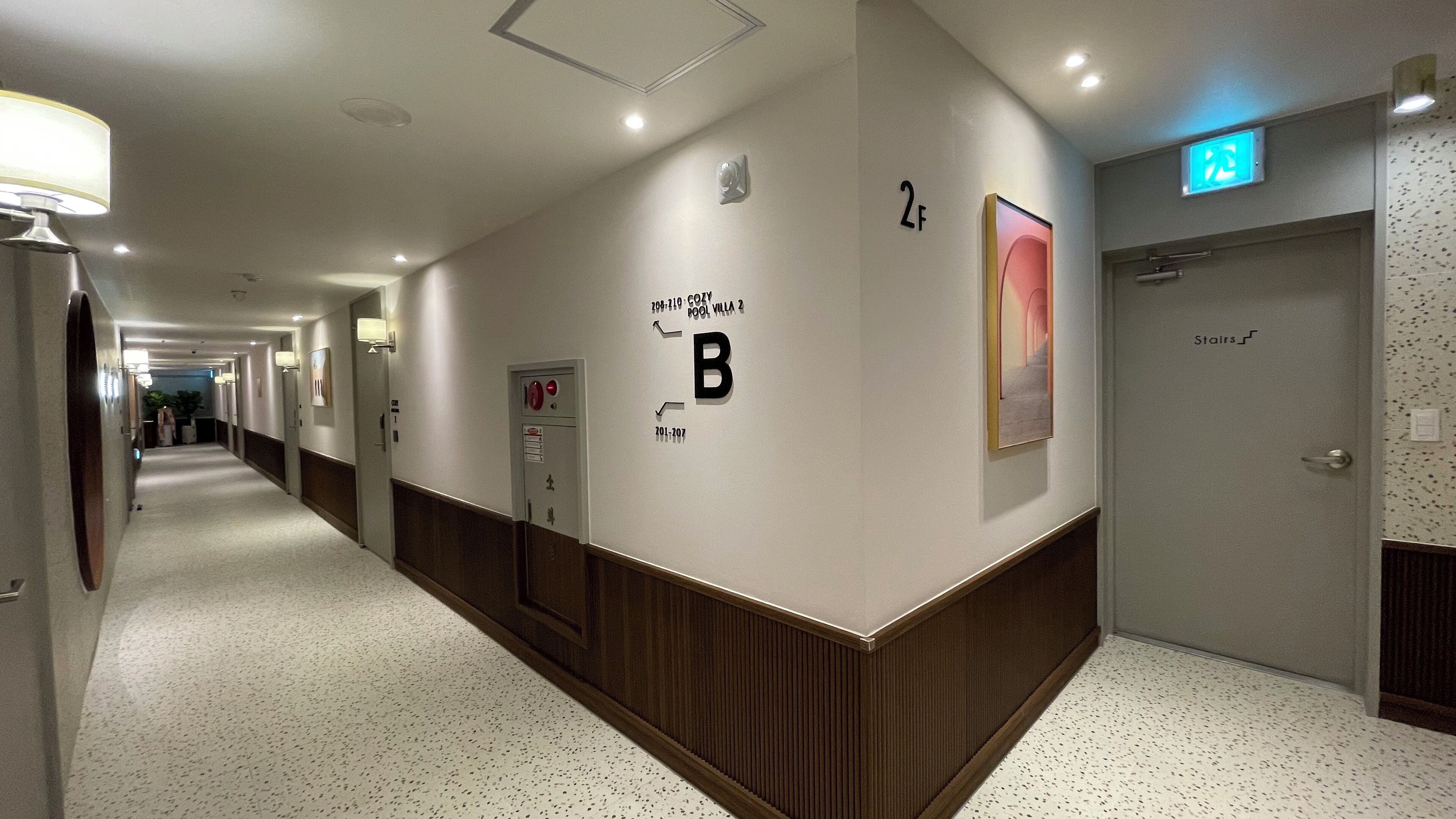 A hotel hallway with a reception desk, a coat check, and an emergency exit sign.