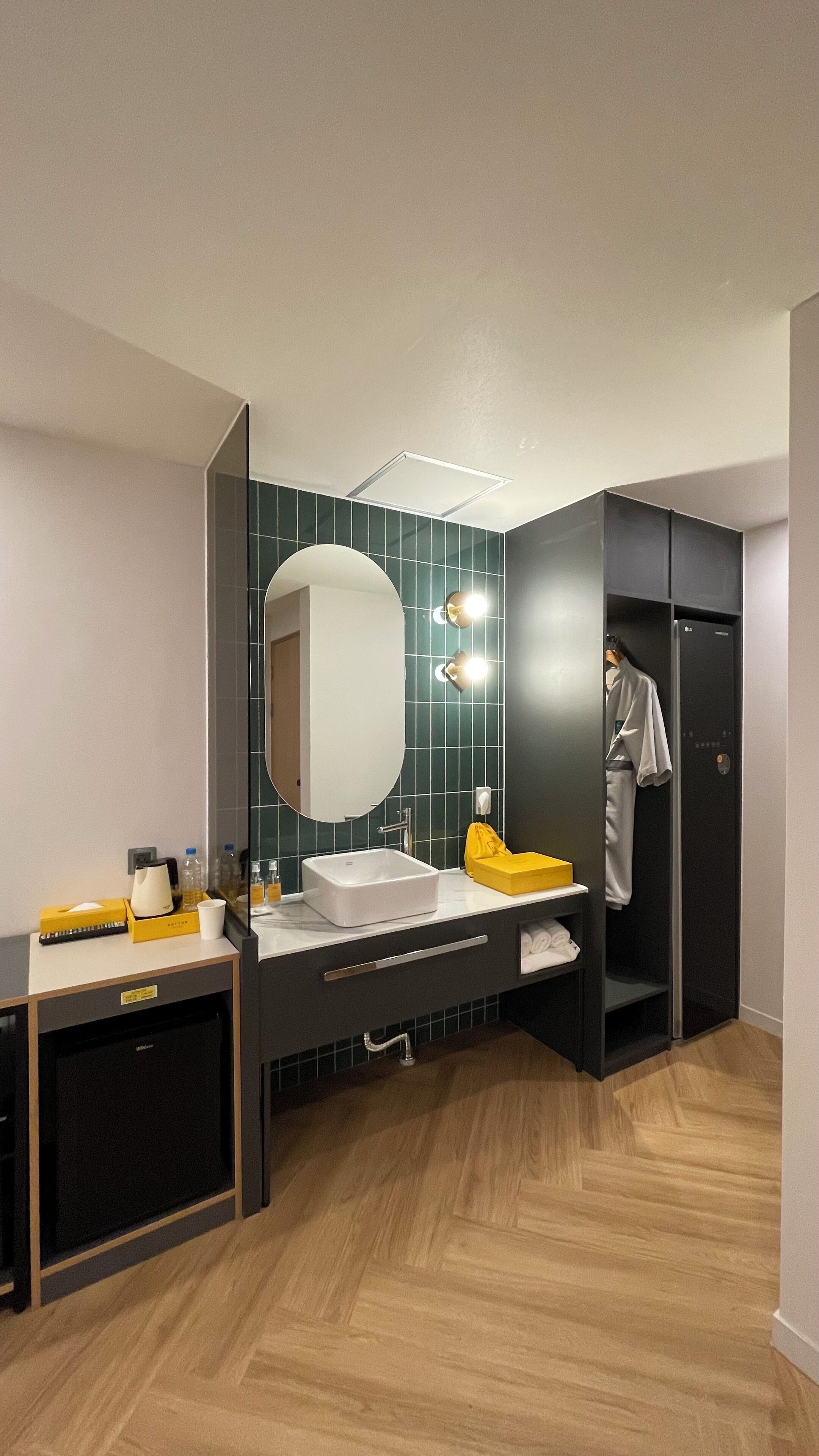 A modern bathroom with a white sink, mirror, and yellow towel. There is a black cabinet and a wooden floor.