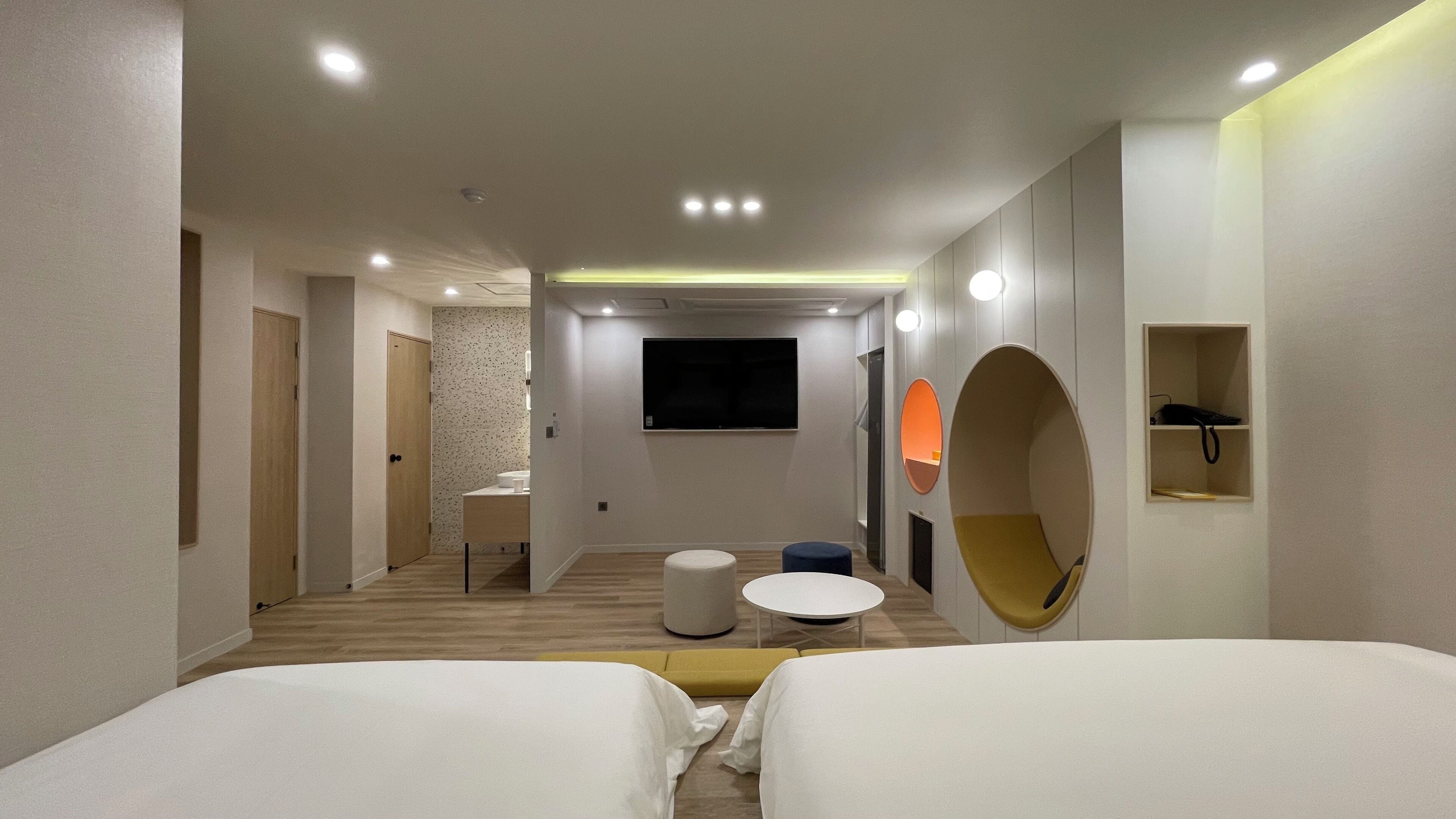 Una habitación de hotel con dos camas, una mesita redonda pequeña, un sofá, un televisor y un espejo.
