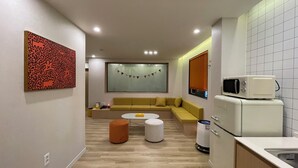 Um espaço compacto com sofá, uma mesinha redonda, micro-ondas e lixeira.
