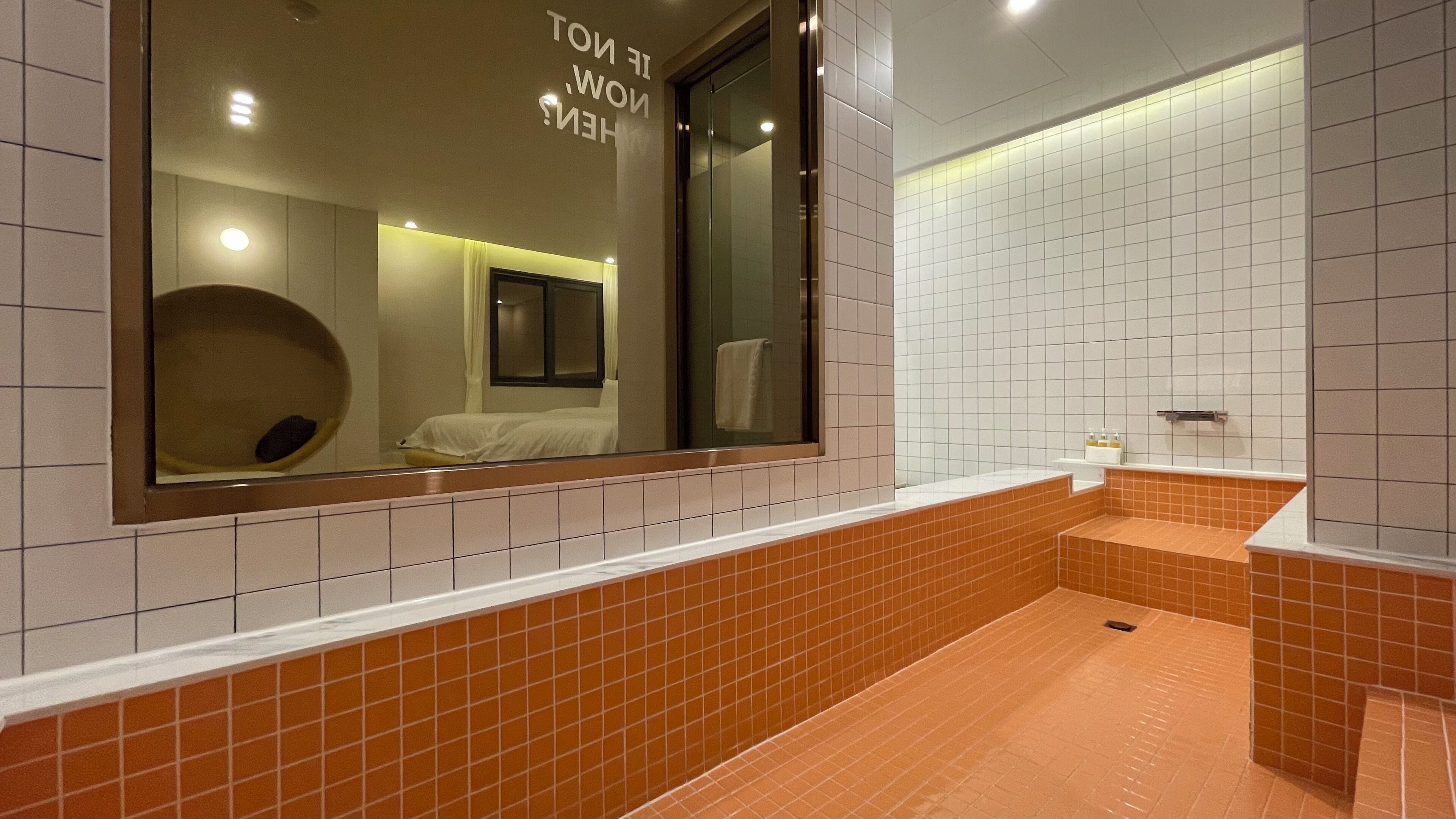 A modern bathroom with a large mirror, a small window, and a tiled floor.