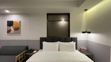 A hotel room with a bed, bedside table, chair, and a painting on the wall.