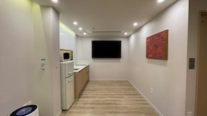 Un pasillo estrecho con una zona de cocina a la izquierda, un televisor de pantalla plana en la pared y una obra de arte con diseño a la derecha.