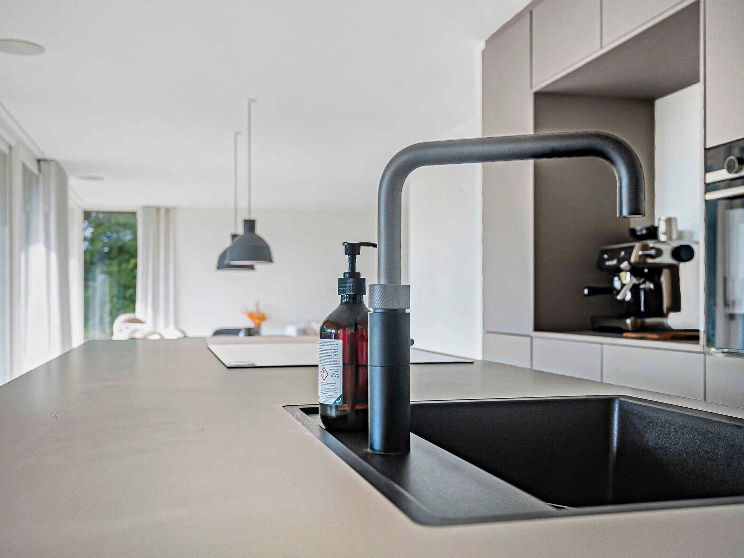 A modern kitchen with a sleek faucet, a bottle of hand sanitizer, and a pendant light.