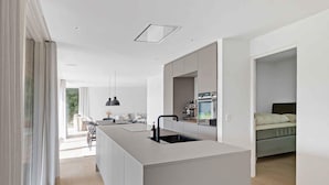 A modern kitchen with a central island, a dining area with a table and chairs, and a bedroom with a bed. - 5 Star Holiday Home in Aakirkeby (Akirkeby)