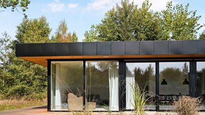 A modern house with large glass windows, a wooden deck, and a metal roof. - 5 Star Holiday Home in Aakirkeby (Akirkeby)