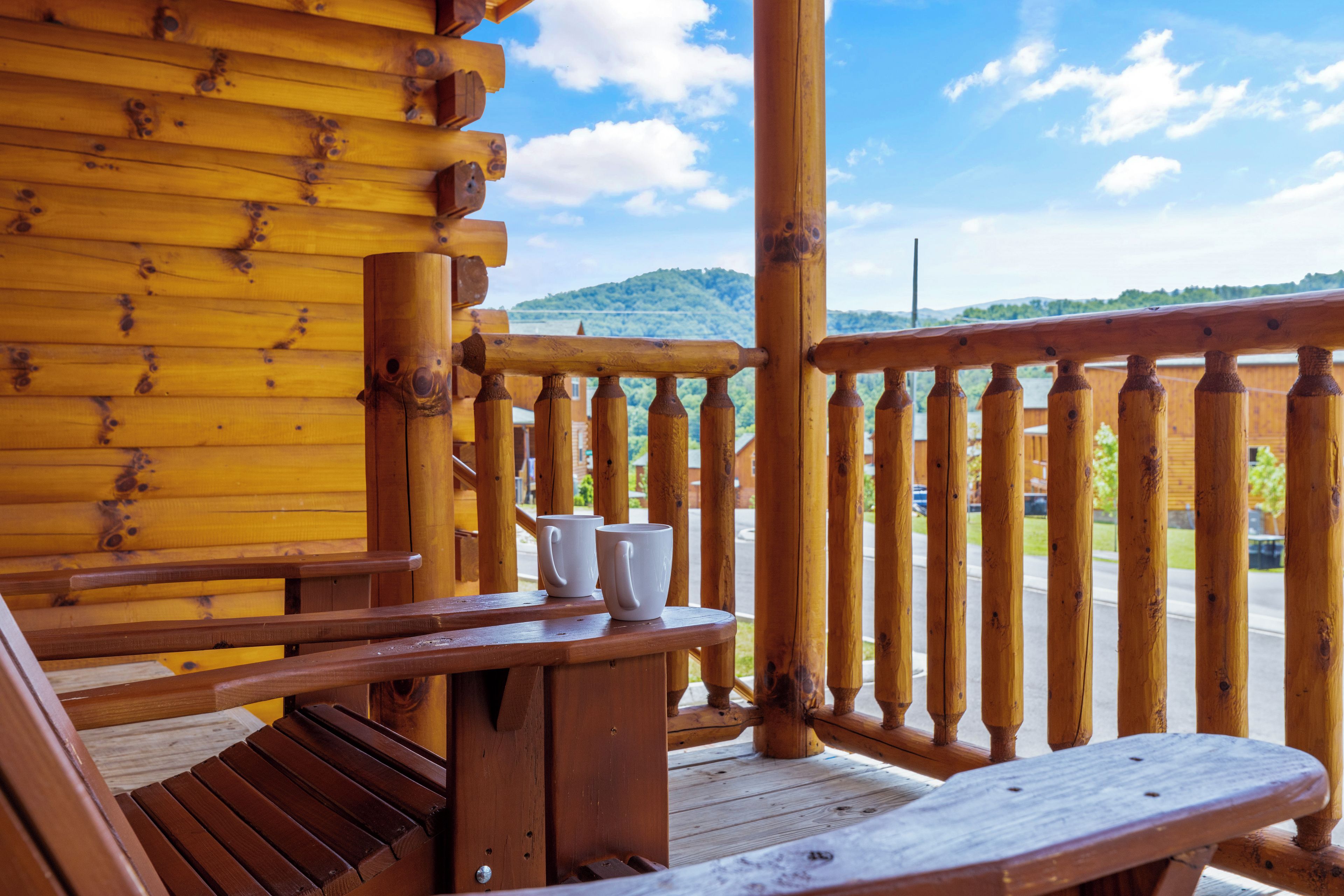 A wooden deck with a railing, a bench, and two white cups on a table.