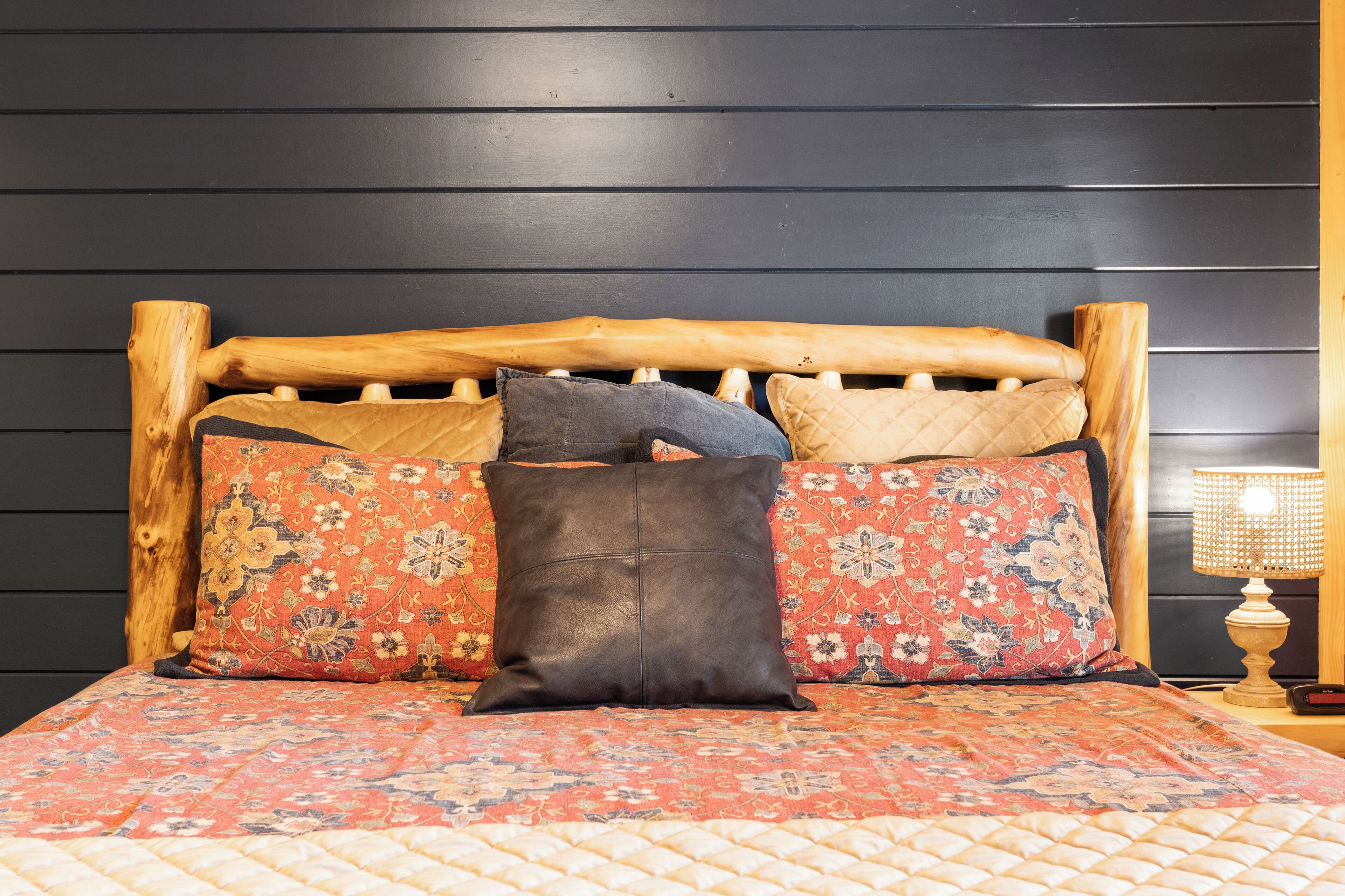 Una cama con cabecera de madera, varios cojines estampados y una colcha acolchada.