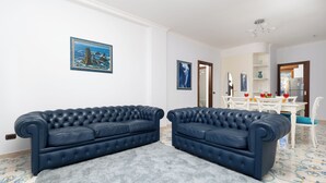 A living room with two dark blue leather sofas, a white dining table with chairs, and a grey rug. - Casa Cafarelli (Sorrento)