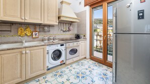 A compact kitchen with wooden cabinets, a washing machine, and a refrigerator. - Casa Cafarelli (Sorrento)
