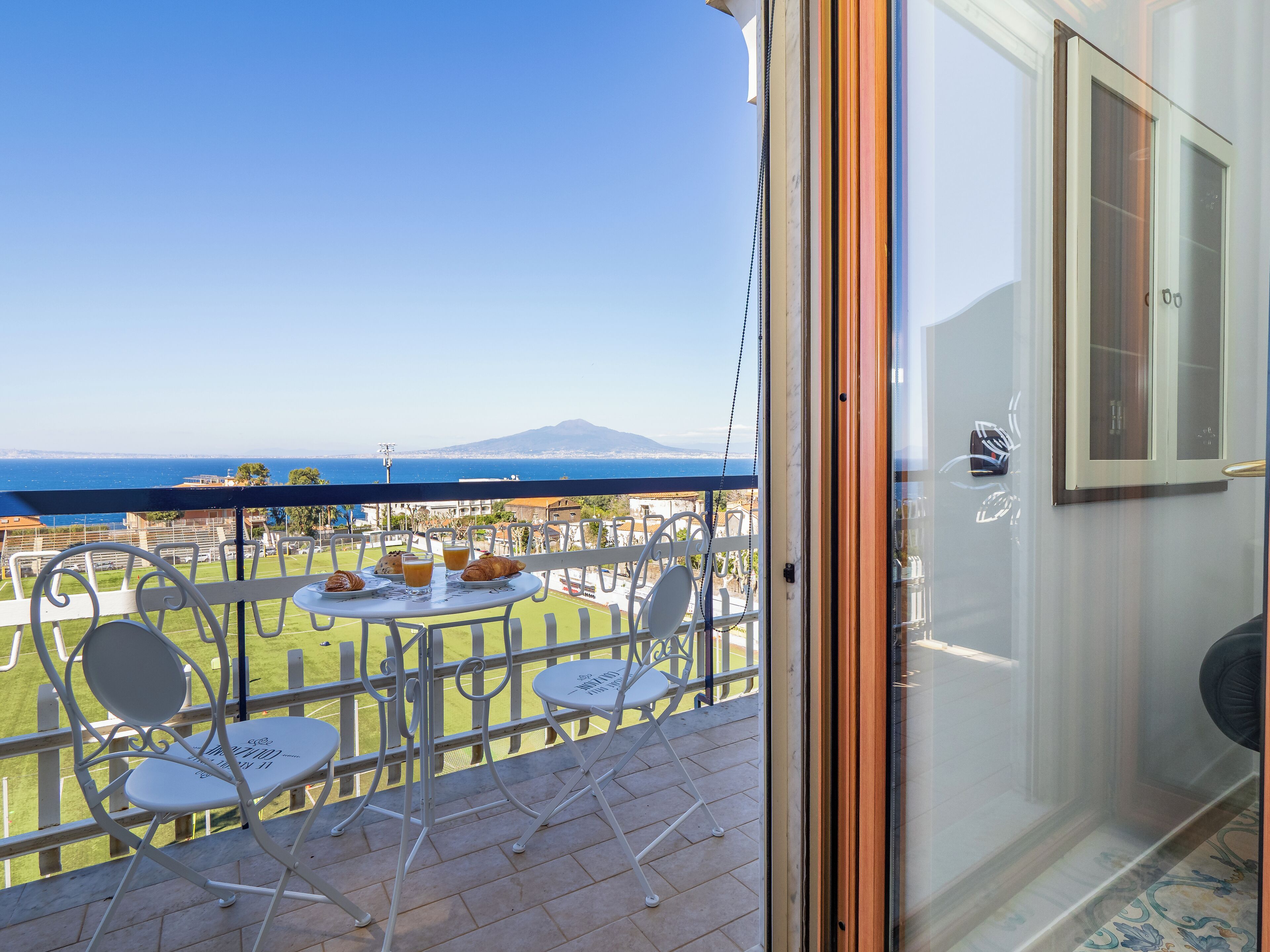 Ein Balkon mit Tisch für zwei Personen, mit Blick auf eine malerische Seelandschaft und ein Gebirge.