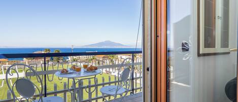 Ein Balkon mit Tisch für zwei Personen, mit Blick auf eine malerische Seelandschaft und ein Gebirge.