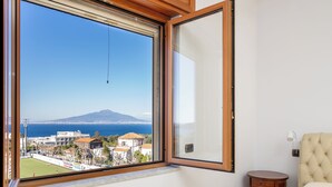 A bedroom with a large window offering a view of a coastal town and a mountain. - Casa Cafarelli (Sorrento)