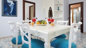 A dining area with a white table, blue upholstered chairs, and a fruit bowl with oranges and lemons. - Casa Cafarelli (Sorrento)