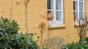 A yellow building with two white-framed windows and a small ledge below them. - 5 Star Holiday Home in Ronne (Ronne)