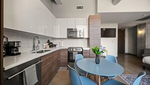 Une cuisine moderne avec des meubles blancs, un four à micro-ondes et une cuisinière. On y trouve une table à manger bleue, quatre chaises et un vase rempli de fleurs.