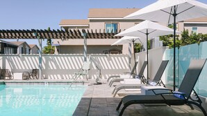 A pool area with lounge chairs and umbrellas, surrounded by a building with a tiled roof and a pergola.