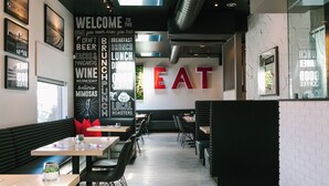 A modern restaurant interior with a central wall displaying the word "EAT" in large letters, surrounded by various food and drink options listed on the walls.
