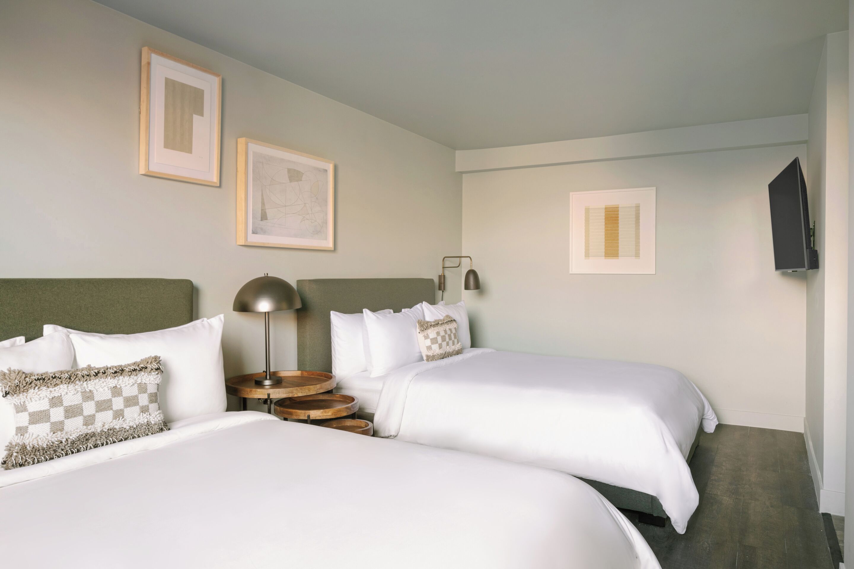 Une chambre d’hôtel avec deux lits, une table de chevet, une lampe et des œuvres d’art encadrées accrochées au mur.