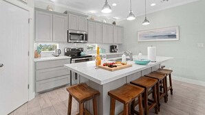 Una cocina moderna con armarios blancos, una isla central con taburetes, un microondas y una cafetera.