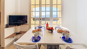 Un comedor con un televisor a la izquierda, una mesa dispuesta con platos, vasos y una botella de refresco.