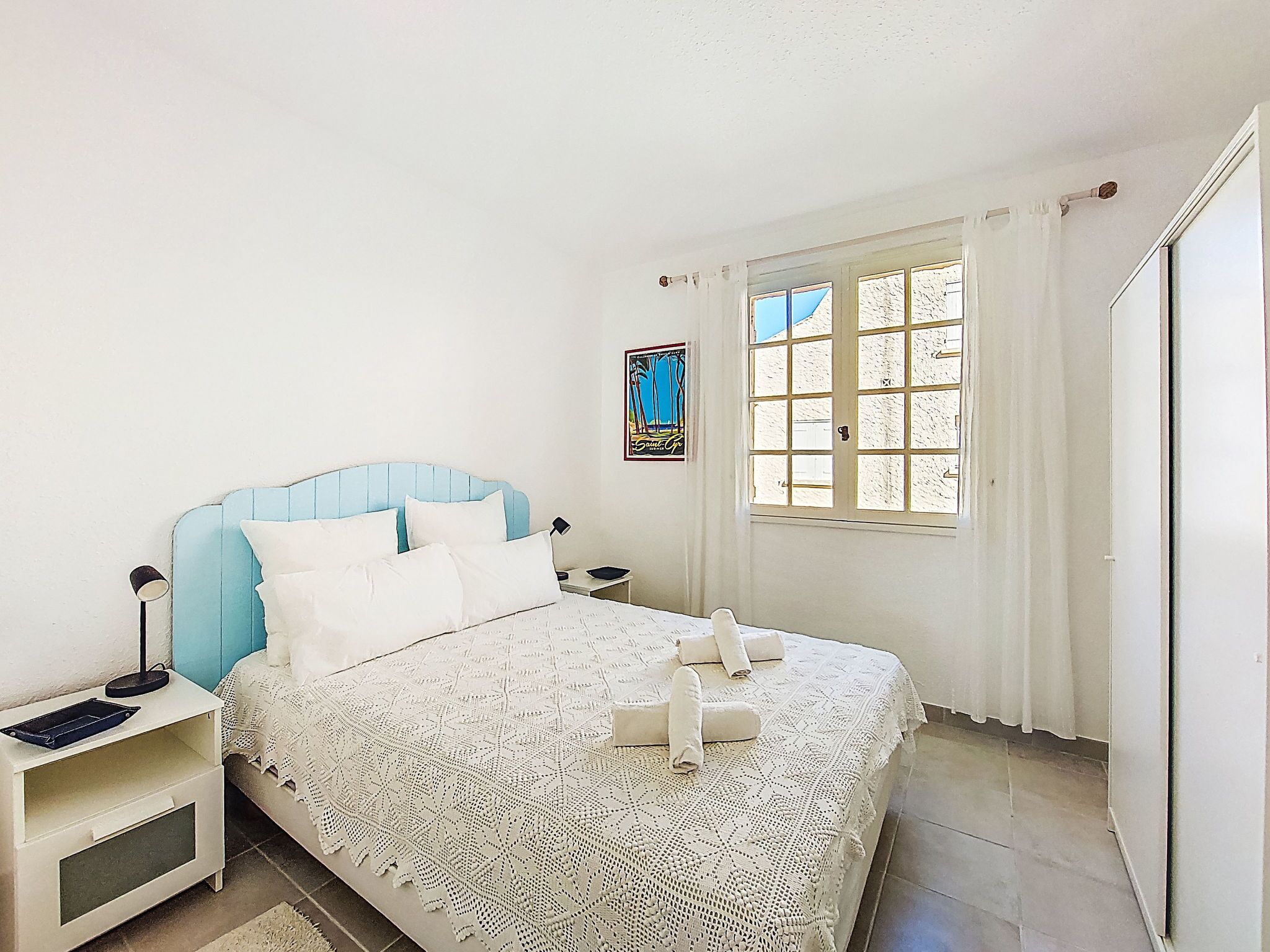 Un dormitorio con cama, mesita de noche, ventana con cortinas y un adorno en la pared.