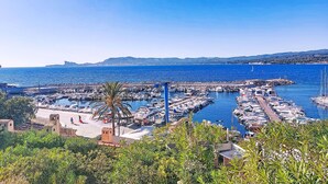 Un puerto deportivo con barcos amarrados, cielo azul despejado y una cadena montañosa en la distancia.