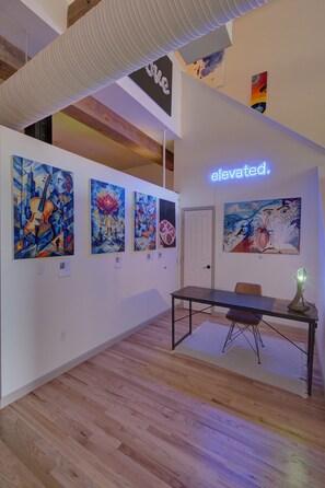 Uma galeria de arte com soalho de madeira, uma mesa central e várias pinturas abstratas nas paredes.