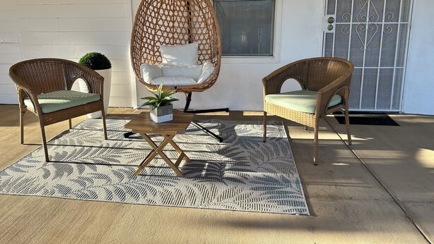 A patio with two wicker chairs, a hanging chair, a small potted plant, and a patterned rug.