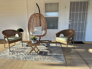 Eine Terrasse mit zwei Korbstühlen, einem Hängesessel, einem kleinen Topfpflanzen und einem gemusterten Teppich.